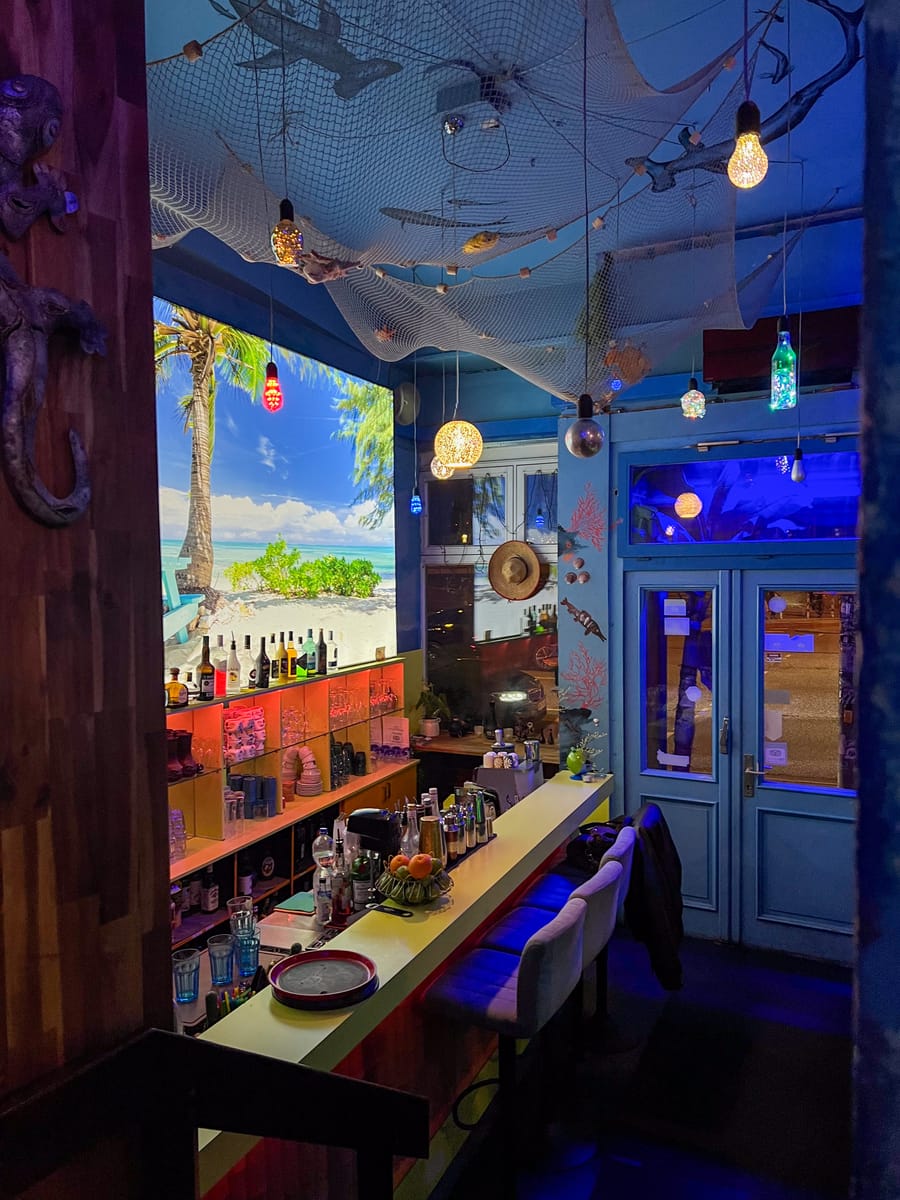 Die Bar: Holztheke, Flaschenregal und blaues Licht unter Muschel-Leuchtern