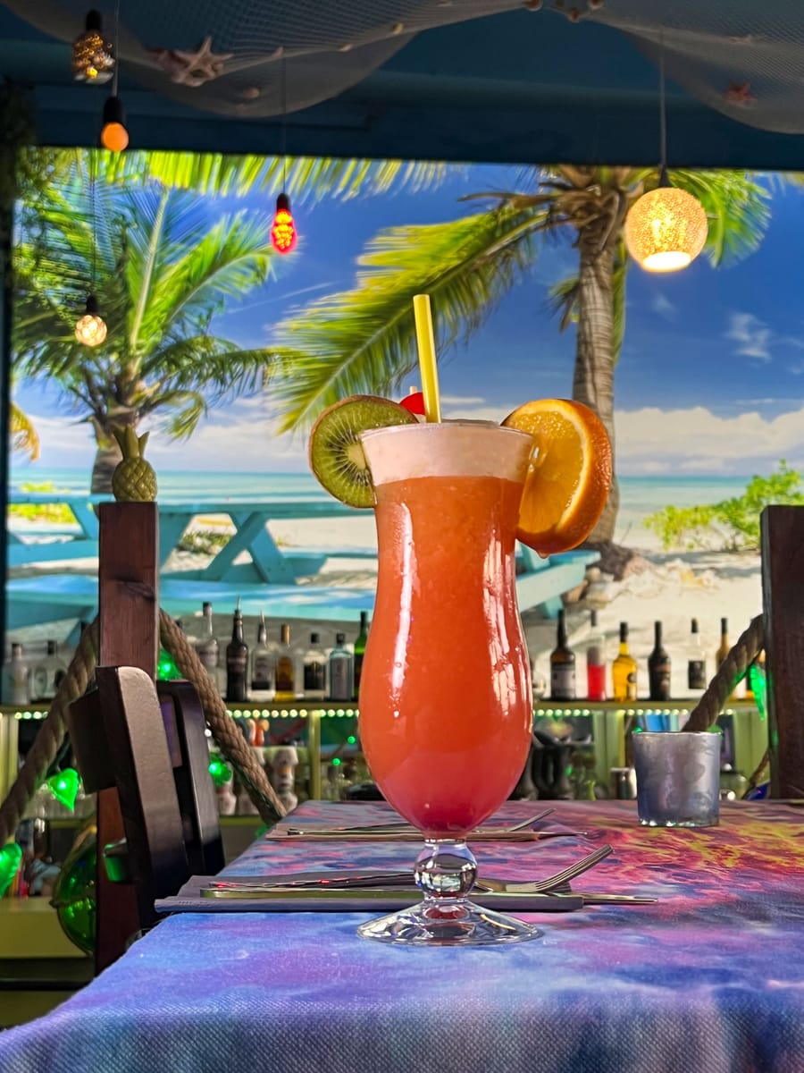 Ein roter Cocktail mit Kirsche vor dem gemalten Strand mit Palme